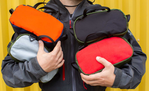 Person holding four Grab Bags that will be offered on 10/13. Clockwise: Black 420 2x2, Red Microsuede, Silver 500d, and Comeback Orange.